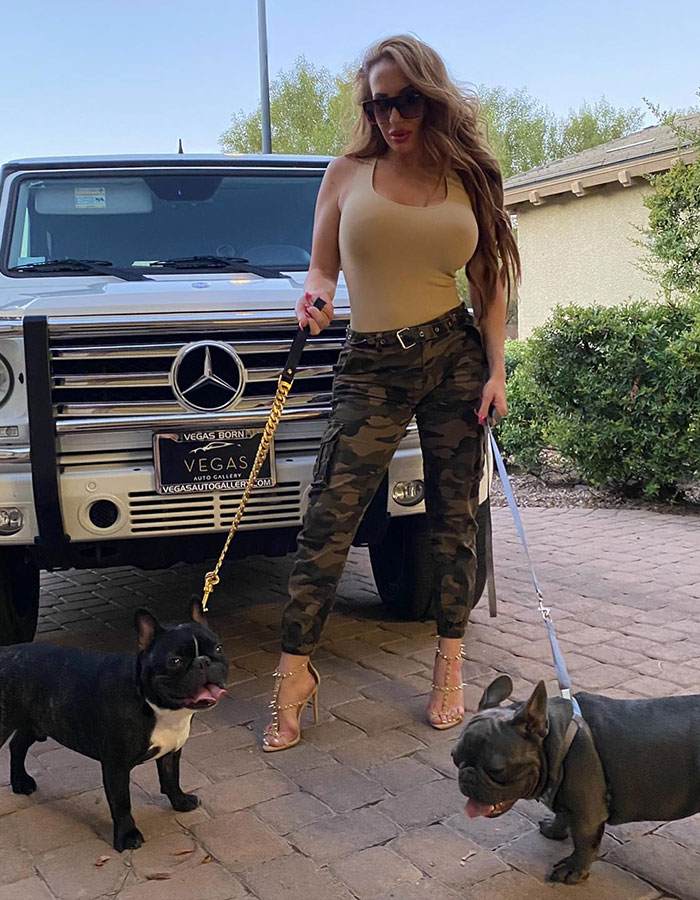 Adult star with two dogs in front of a Mercedes SUV, wearing sunglasses and camo pants.