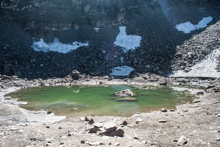 Mysterious green lake surrounded by rocky terrain and patches of snow, showcasing an unsolved mystery.