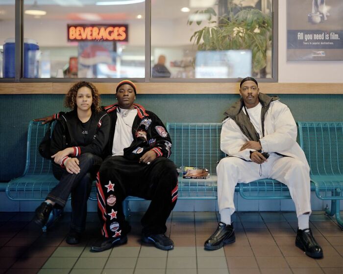 Three people seated on a bench at a bus stop, captured in a candid photo documenting life at America’s bus stops.
