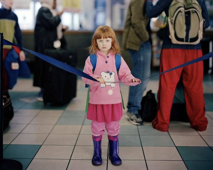 Young girl in pink outfit standing inside a bus station, capturing life at America’s bus stops by photographer.