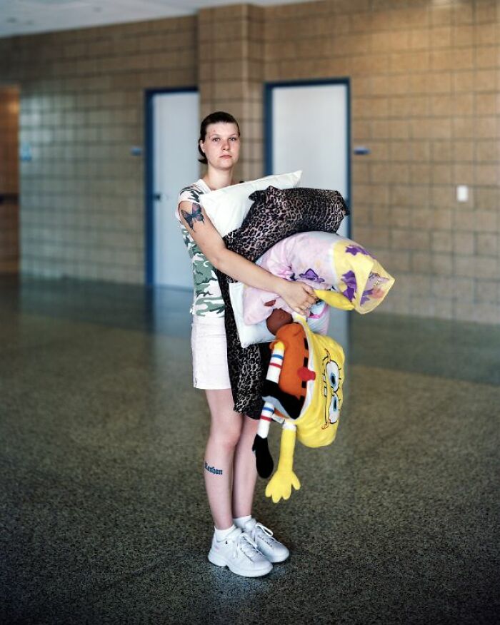 Young woman holding pillows and stuffed toys, captured by photographer documenting life at America’s bus stops.