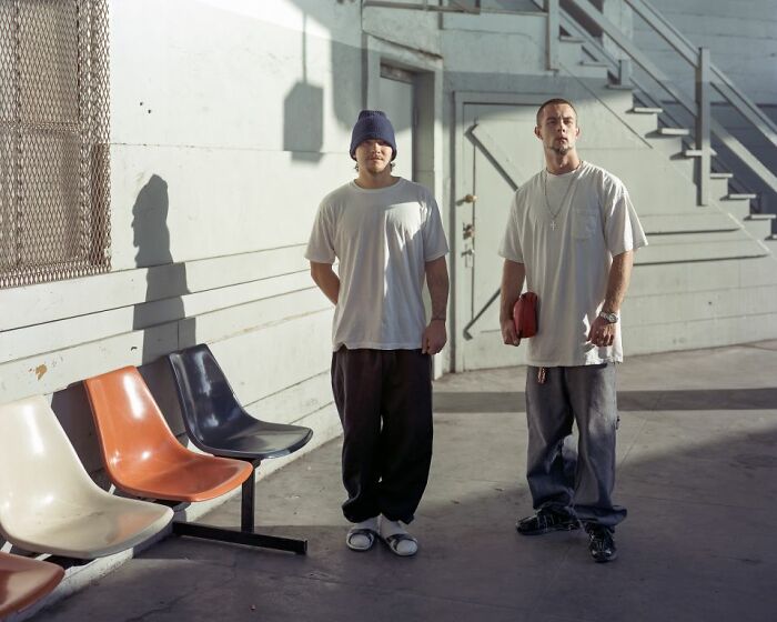 Two young men standing near empty colored seats at an urban bus stop, capturing life at America’s bus stops.