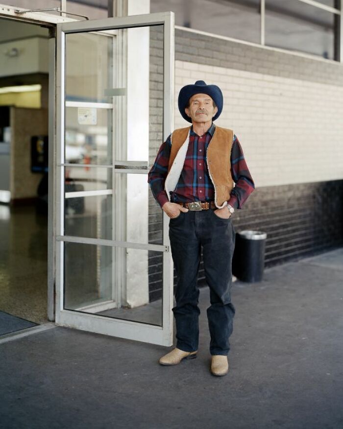 Man wearing cowboy hat and vest standing at America bus stop, captured by photographer documenting life at bus stops.