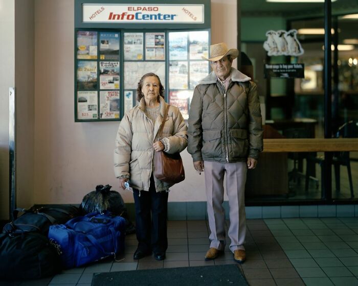 An elderly couple standing with bags at an America bus stop, captured in a photo documenting life at bus stops.