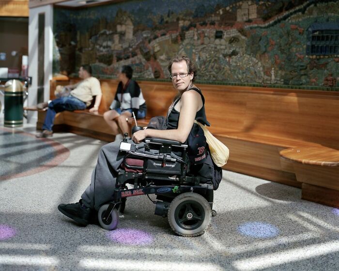 Man in a motorized wheelchair at a bus stop, captured by a photographer documenting life at America’s bus stops.