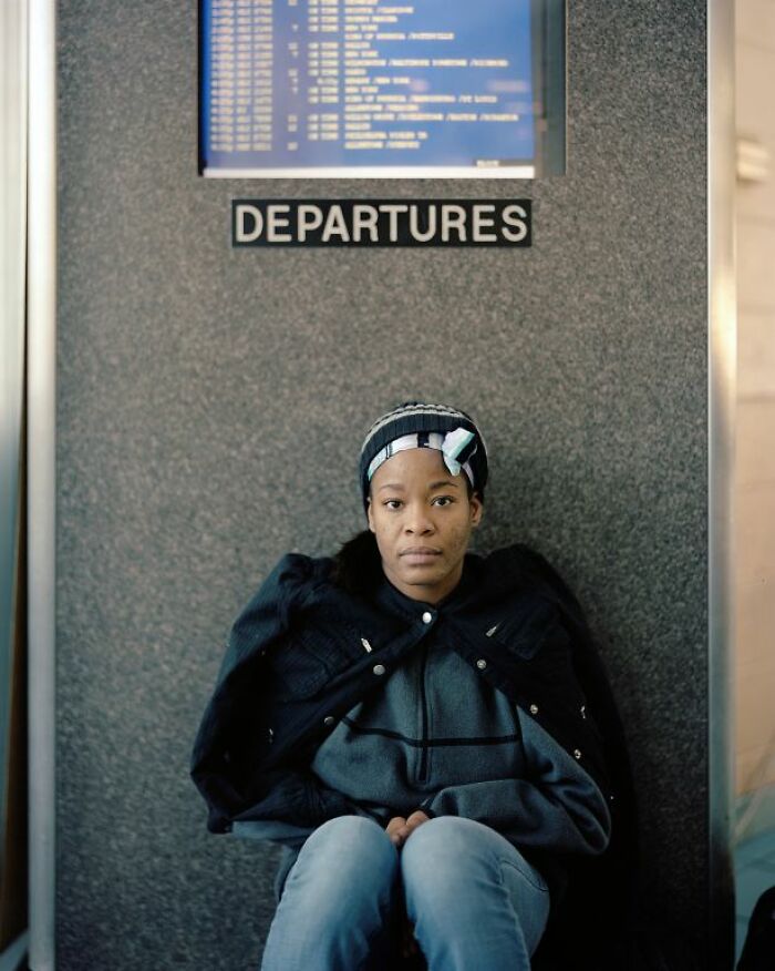 Woman sitting at a bus stop under departures sign, captured in documentary style showing life at America’s bus stops.