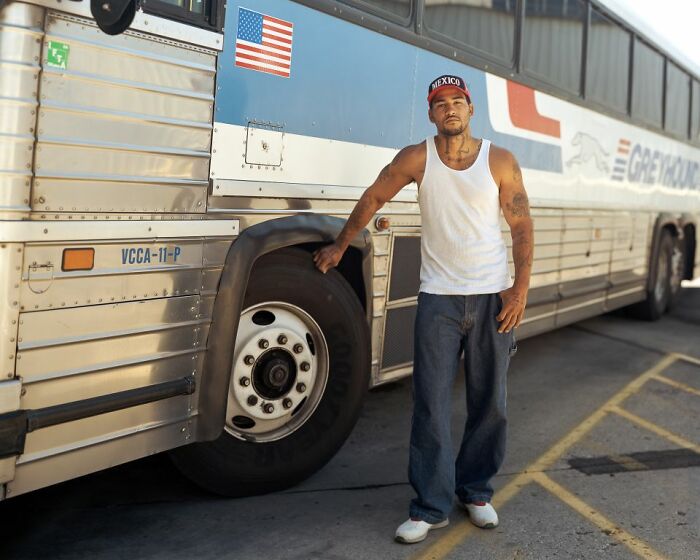 Man in a tank top and cap standing by a bus, captured by photographer documenting life at America’s bus stops.