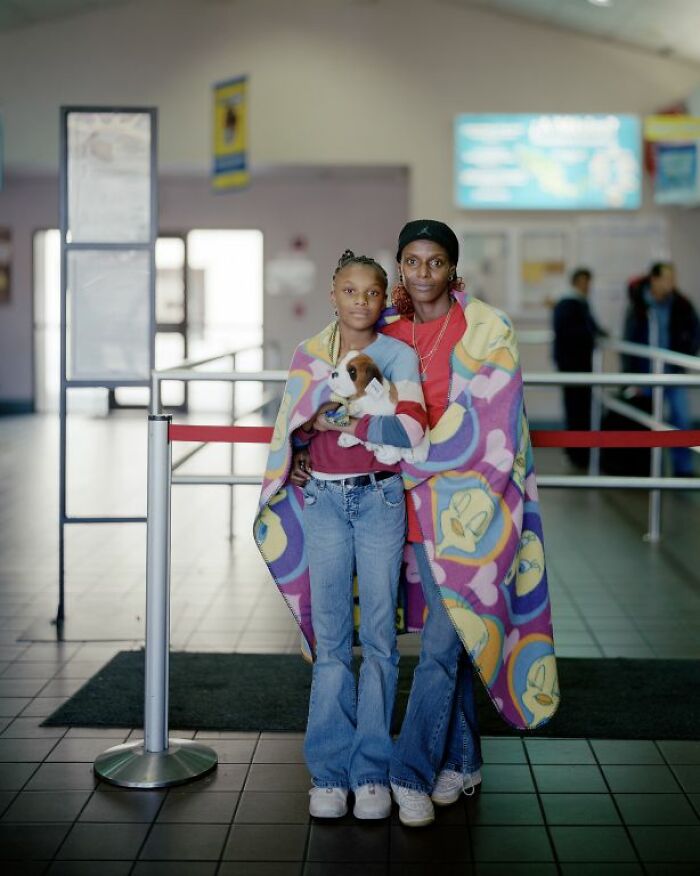 Two people wrapped in a colorful blanket holding a puppy, captured in a photo documenting life at America's bus stops.