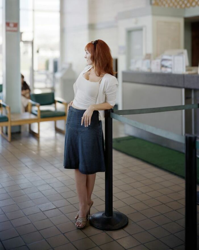 Woman with red hair leaning on a barrier inside a bus station, capturing life at America’s bus stops.