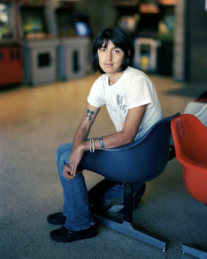 Young person with tattoos sitting in a bus stop chair, captured in a candid moment documenting life at America’s bus stops.