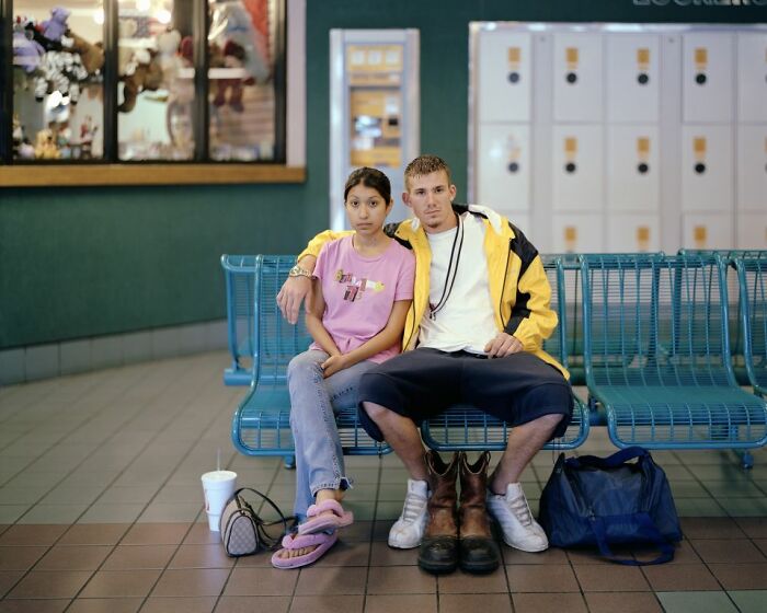Two people sitting closely on a bench at an America bus stop, capturing life and moments documented by photography.