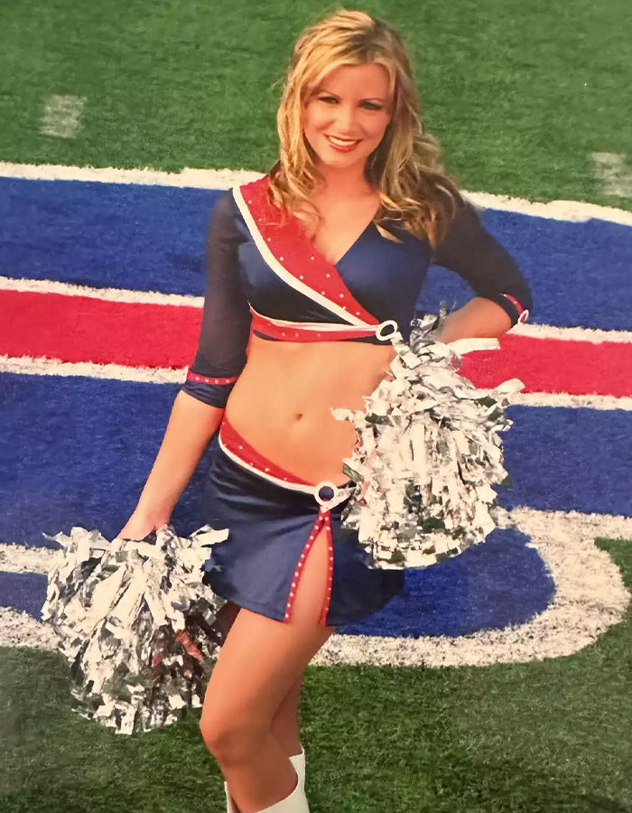 Cheerleader in blue and red uniform holding pom-poms on a football field, Buffalo Bills logo visible. Cheerleader in blue and red uniform holding pom-poms on a football field, Buffalo Bills logo visible.