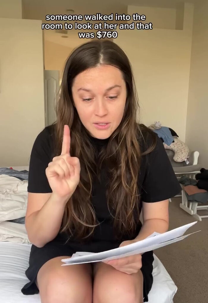 Woman surprised by large hospital bill for baby, holding papers and gesturing with finger in a room.