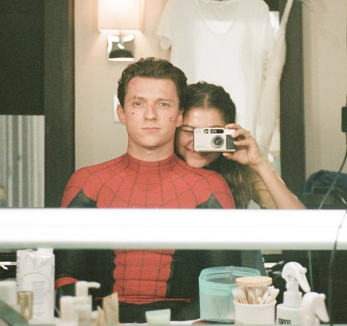 Zendaya and Tom Holland taking a playful mirror selfie, with Holland dressed as Spider-Man, capturing a romantic moment.