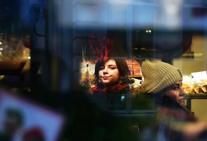 Nadia Eeckhout captures an everyday moment of two people through a window, with warm indoor lighting.