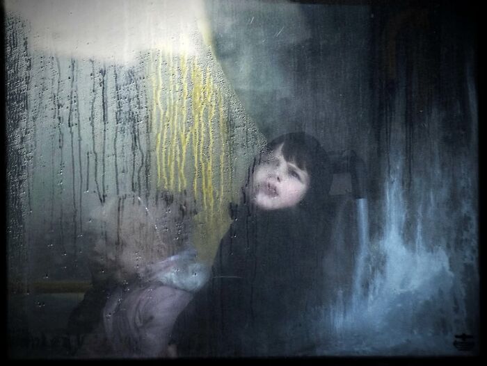 Children with blurred faces seen through a rainy window, captured by Nadia Eeckhout’s lens.