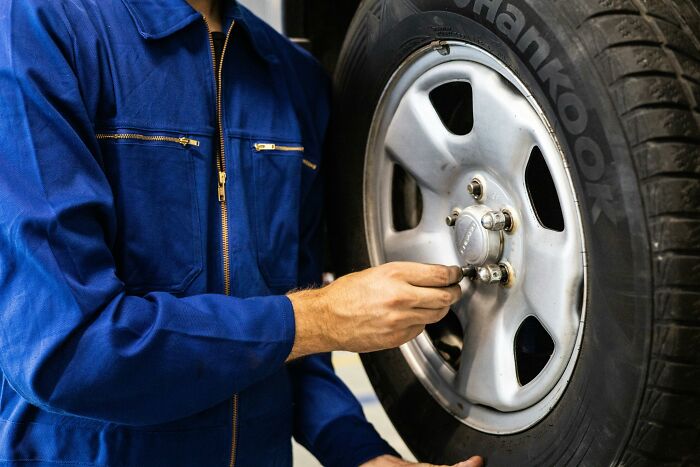Person in blue coveralls tightening a car wheel bolt, essential for road trip safety and preparation. Person in blue coveralls tightening a car wheel bolt, essential for road trip safety and preparation.