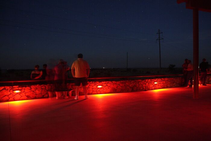 People standing near a wall under red lights at night, possibly observing weird unsolved mysteries.