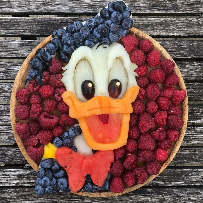 Healthy eating art: a fruit platter designed as a cartoon character with blueberries and raspberries on a wooden table.