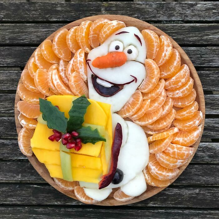 Healthy eating art with character made from fruits like oranges and mango, arranged on a round wooden plate.