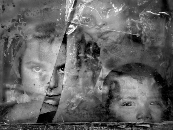 Children looking through a c*****d window, captured by Istvan Kerekes, showcasing resilience and beauty of everyday people.