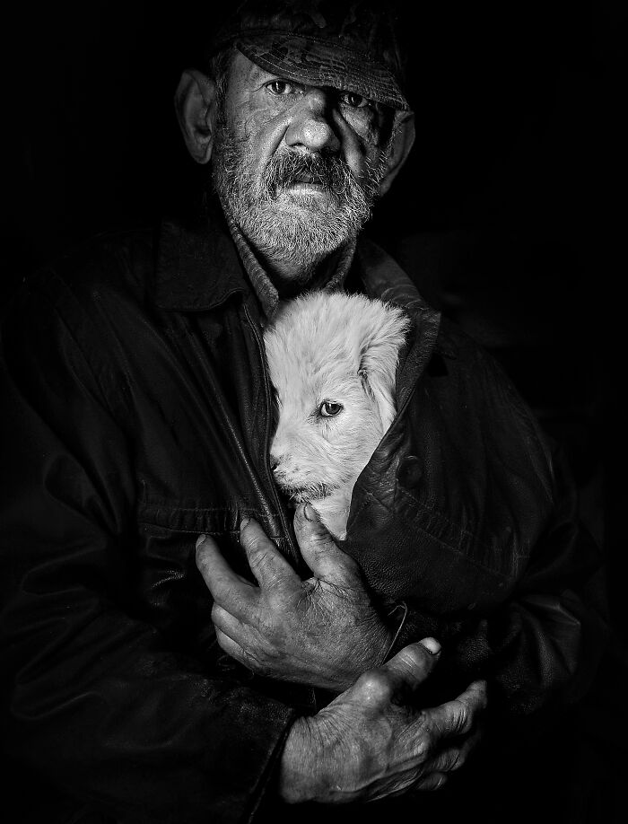 A man holds a puppy inside his jacket, showcasing the resilience and beauty of everyday people in Istvan Kerekes' photography.