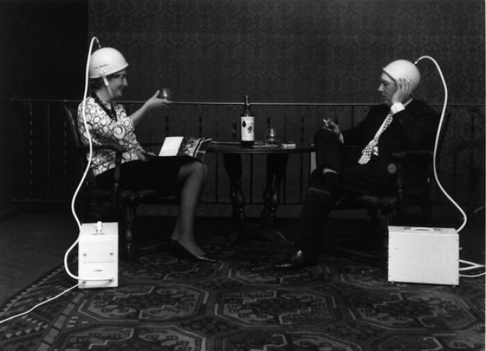 Two people wearing helmets with cables, sitting at a table, illustrating historical inventions ahead of their time.