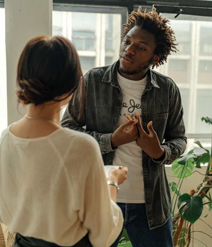 People in conversation by a window; one gestures while talking, possibly discussing signs of feigned maturity.