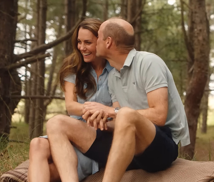 Kate Middleton and Prince William sitting on a picnic blanket, smiling and embracing in a forest setting.
