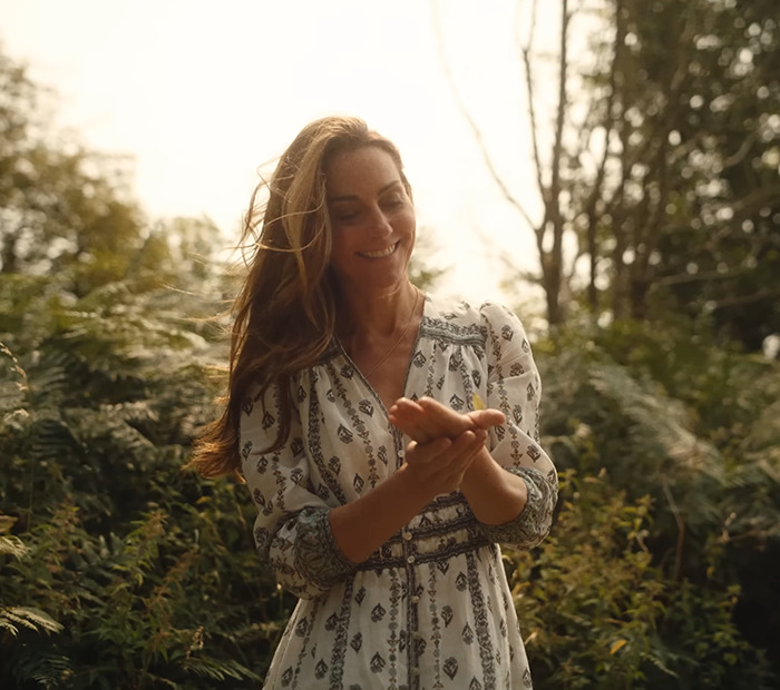 Kate Middleton smiling outdoors in a patterned dress, surrounded by greenery.