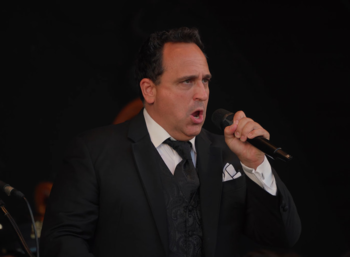 Christopher Macchio in a black suit singing on stage.
