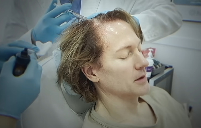 Bryan Johnson receiving longevity medication treatment, seated in a clinic, doctor in white coat and gloves applying injections.
