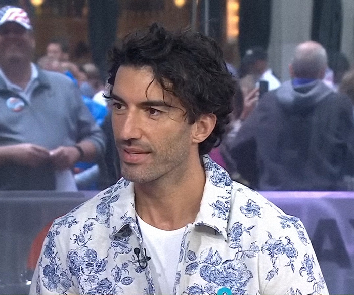 Justin Baldoni in a floral shirt speaking in a public setting.