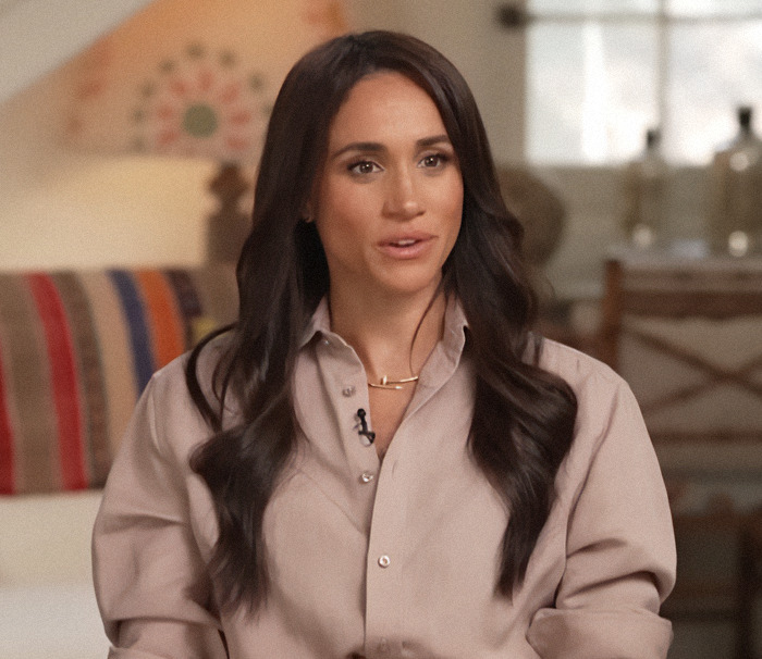 Meghan Markle in a beige shirt sitting indoors. Meghan Markle in a beige shirt sitting indoors.