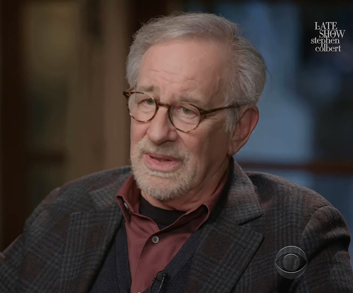 Steven Spielberg with glasses wearing a plaid jacket and maroon shirt on a talk show set. Steven Spielberg with glasses wearing a plaid jacket and maroon shirt on a talk show set.