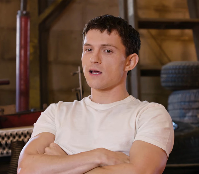 Tom Holland in a white shirt, speaking in a workshop setting.