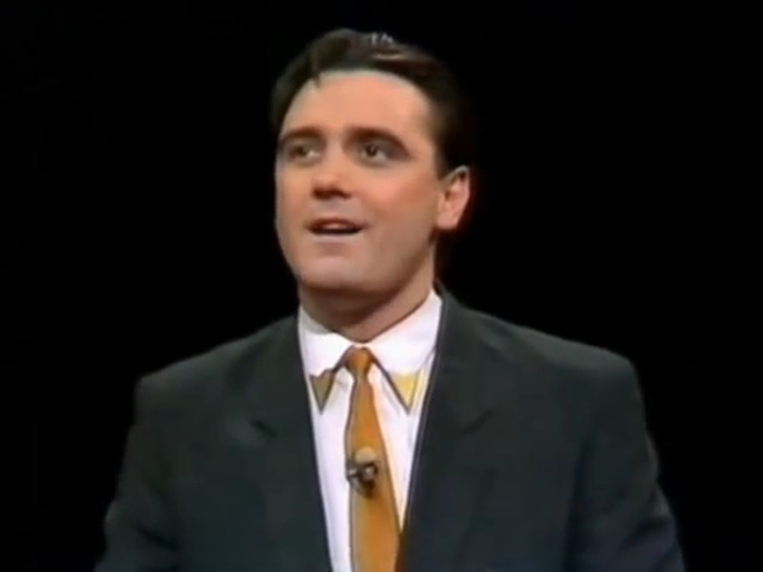 Tony Slattery from 'Whose Line Is It Anyway?', wearing a suit and tie, appearing on stage.