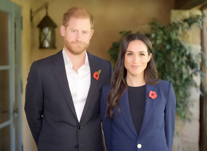 Meghan Markle alongside Prince Harry in a suit, both wearing red poppies. Meghan Markle alongside Prince Harry in a suit, both wearing red poppies.