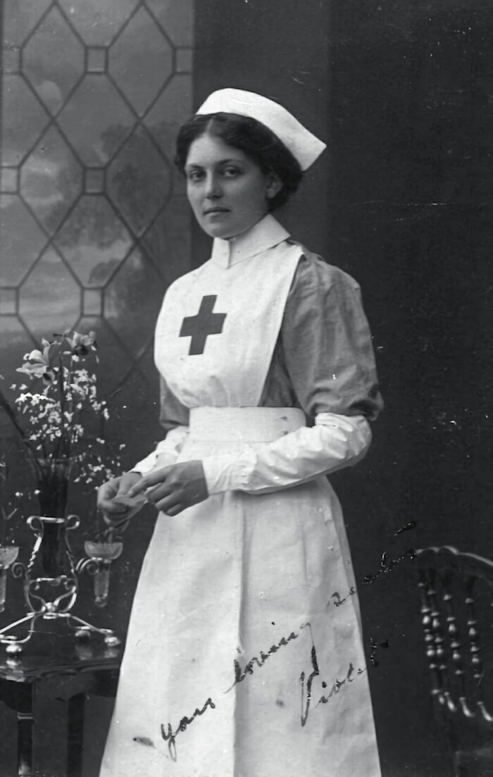 Nurse in historical uniform, representing overlooked historical events, poses beside a table with flowers.