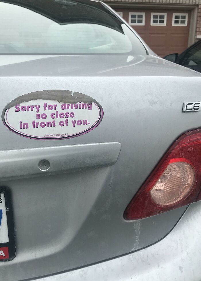 Car with a funny bumper sticker saying, "Sorry for driving so close in front of you," in a parking area.