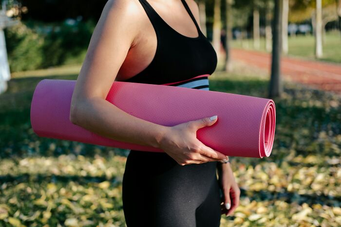 Woman holding pink yoga mat outdoors, proof that affordable items make life easier.