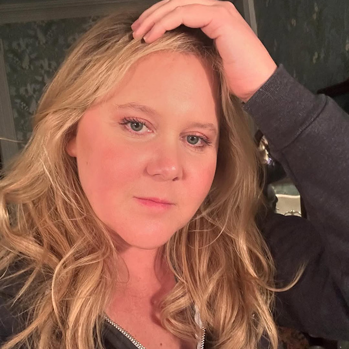 Amy Schumer wearing a dark hoodie in a softly lit room.