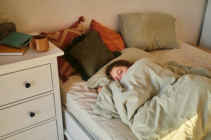 Person sleeping in a cozy bed with pillows, potentially related to reasons for weight gain.