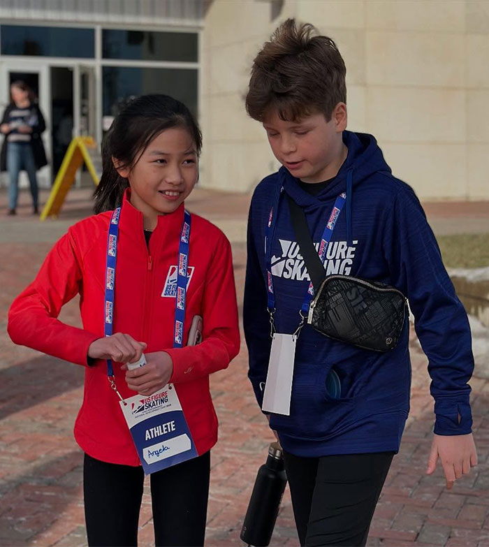 Child ice skating duo walking together, wearing athletic gear with badges. Child ice skating duo walking together, wearing athletic gear with badges.