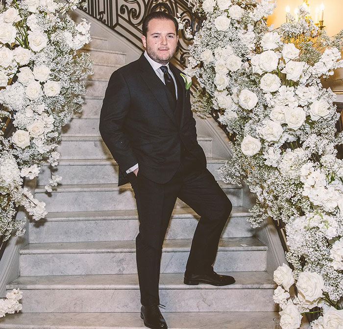 Man in a suit standing on flower-decorated stairs, related to School of Rock child stars reunion.