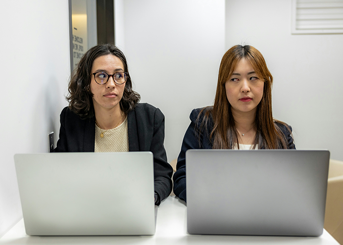 Two women sitting with laptops, one looking concerned; concept of giving notice at work discreetly.