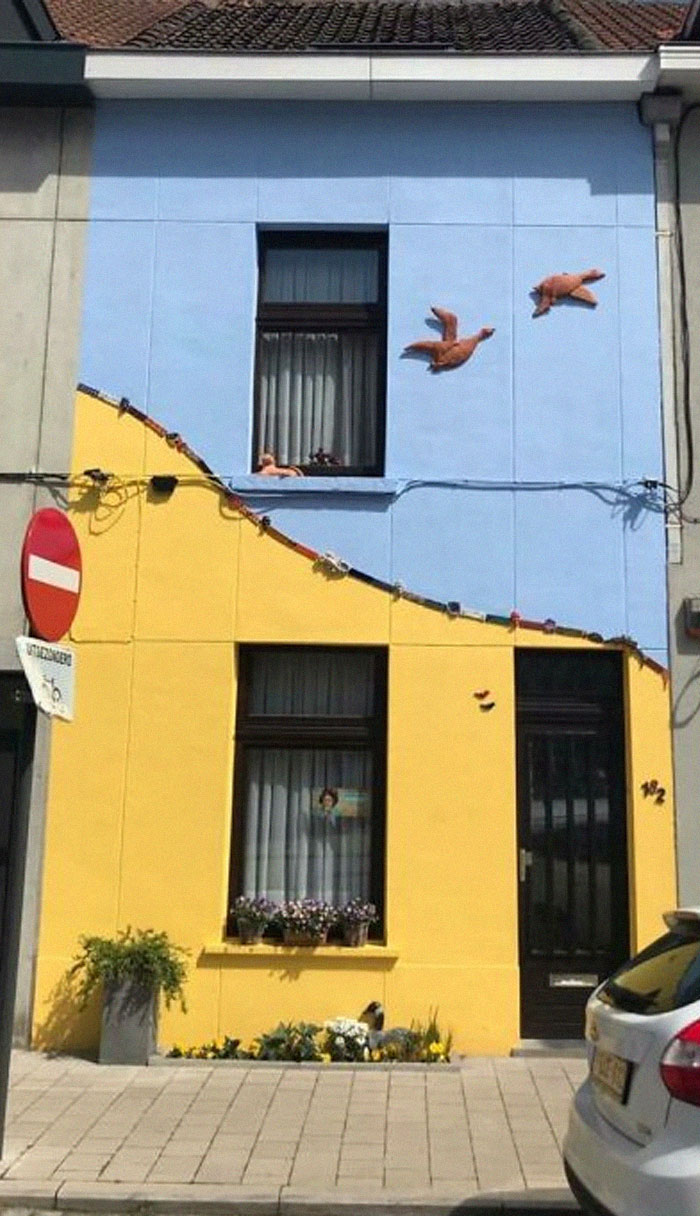 Colorful house with blue and yellow walls, featuring bird sculptures, spotted in Belgium.