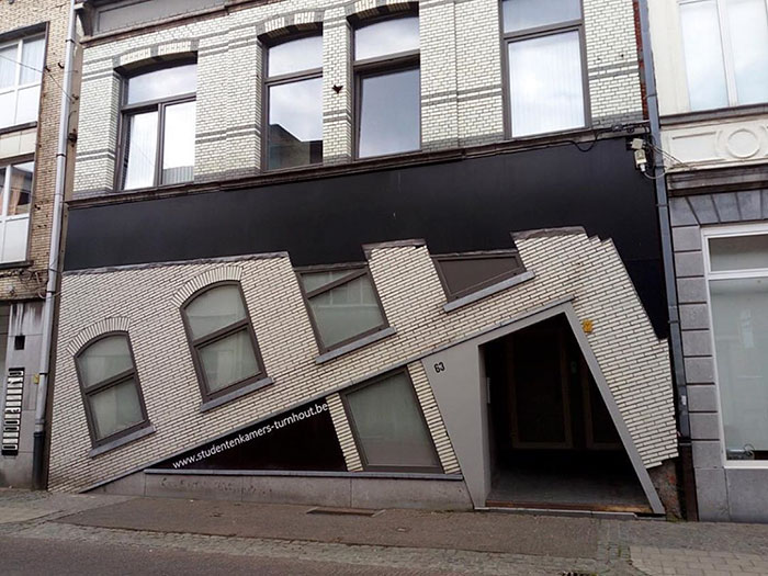 Badly designed house facade with leaning windows and door creating an optical illusion on a city street.