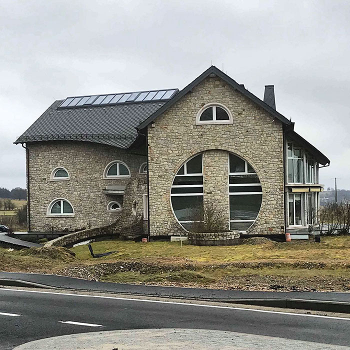 Bad house design with a large circular window and mismatched architectural elements on a cloudy day.