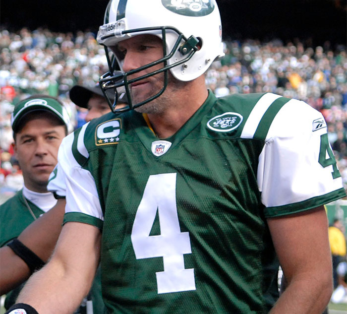 A football player in a green and white jersey with the number 4 stands on the field, surrounded by a cheering crowd.
